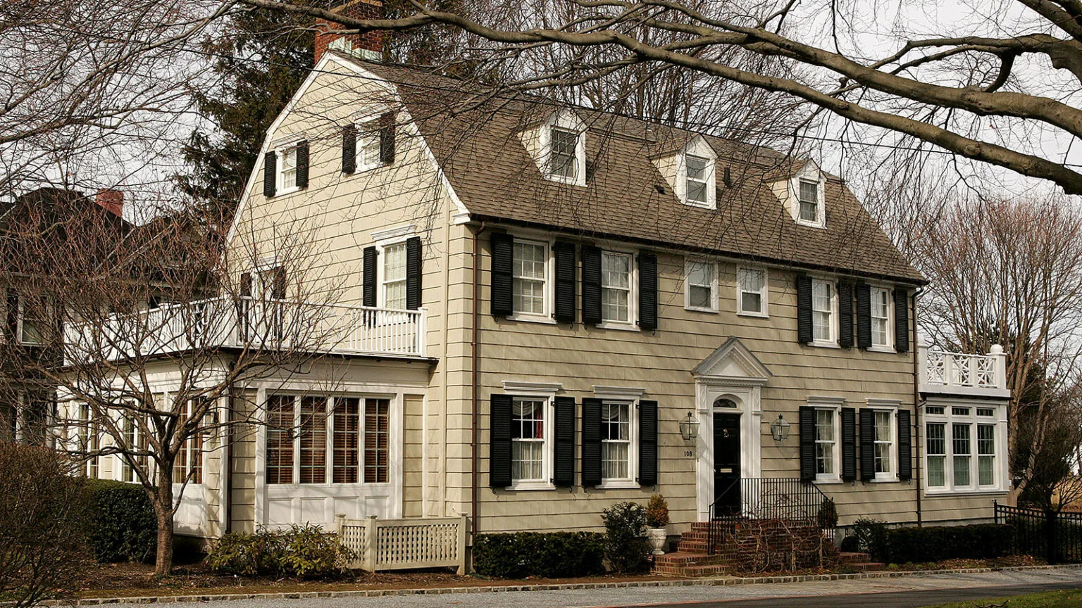 Une grande maison de style colonial hollandais, façade en planche horizontale et blanches avec beaucoup de fenêtres 