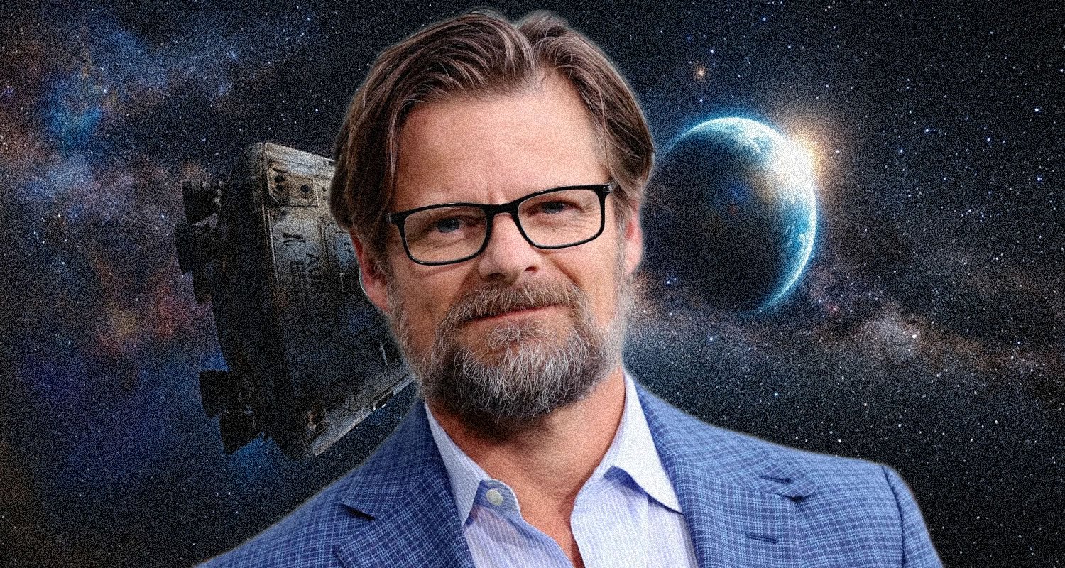 Portrait of a man with glasses in a blue blazer, set against a space backdrop with a distant planet and spacecraft behind him.