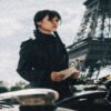 Woman in a black coat stands beside a bicycle, holding a note with the Eiffel Tower visible in the background.