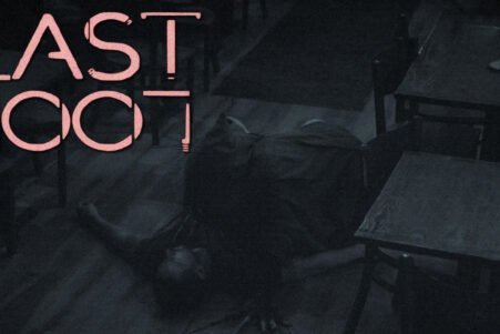 Dim, moody room with large pink neon text saying 'LAST EXIT' and a person crawling on the dark floor beside tables and chairs.