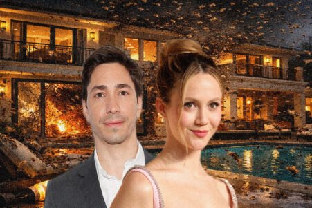 A man in a gray suit and a woman in a pink dress pose in front of a lit luxury house with a pool and falling leaves nearby.