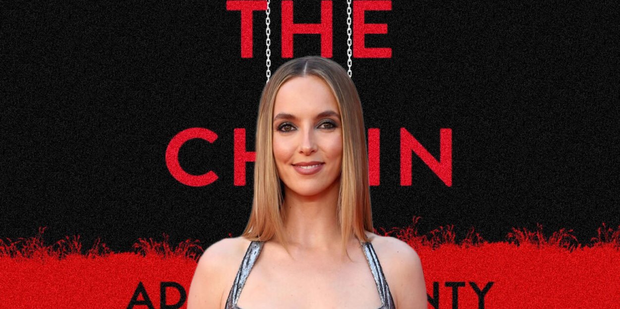 Portrait of a woman on the red carpet, standing in front of a black-and-red poster reading 'THE CHAIN' with hanging chains imagery.