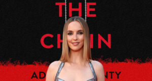 Portrait of a woman on the red carpet, standing in front of a black-and-red poster reading 'THE CHAIN' with hanging chains imagery.