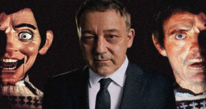 A man in a suit stands between two eerie, oversized mask faces in a dark setting, creating a unsettling portrait