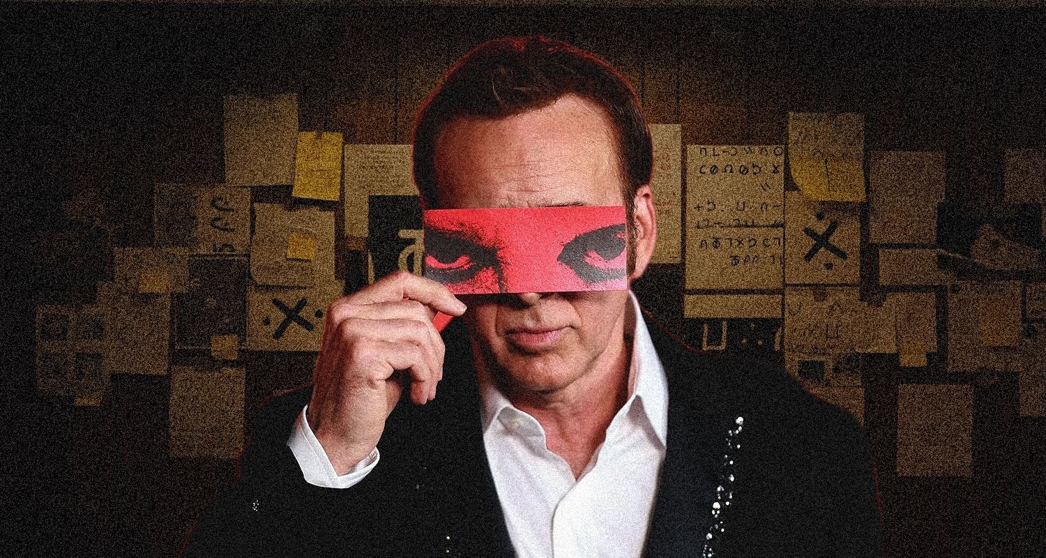 Man in a suit holds a red blindfold over his eyes, standing in a dim room covered with sticky notes and papers behind him.