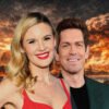 Smiling couple posed in front of a fiery, ruined cityscape backdrop.