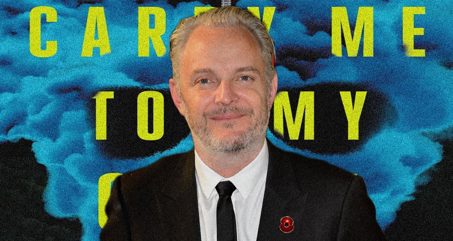 Portrait of a man in a dark suit and tie with a red lapel pin, against a blue smoke backdrop and large yellow text behind him.