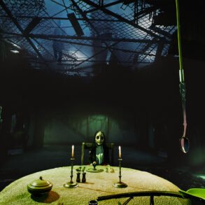 Dim dungeon-like room with a round lace-covered table, lit by candles, and a masked figure seated at the head.