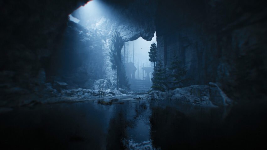 Dark cave interior with a blue glow filtering through an opening; rocky walls, a shallow pool, and distant trees beyond a stairway.