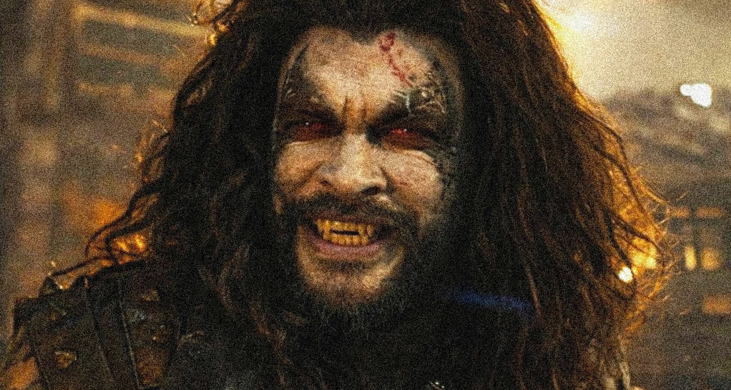 Zombie-like man with long hair, torn forehead wound, and yellowed fangs snarling in a smoky, dimly lit scene.